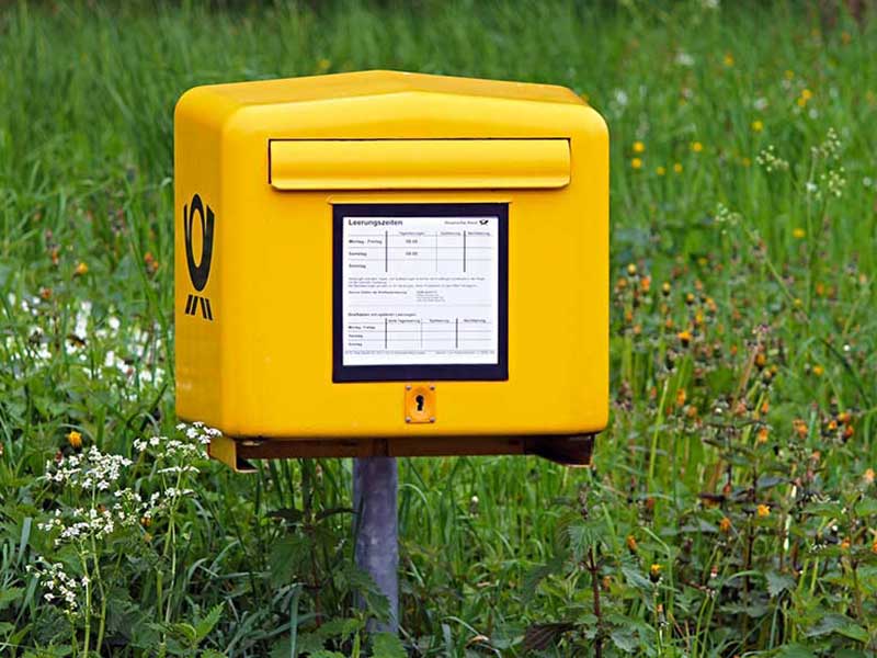 Ein gelber Briefkasten vor einer grünen Wiese.
