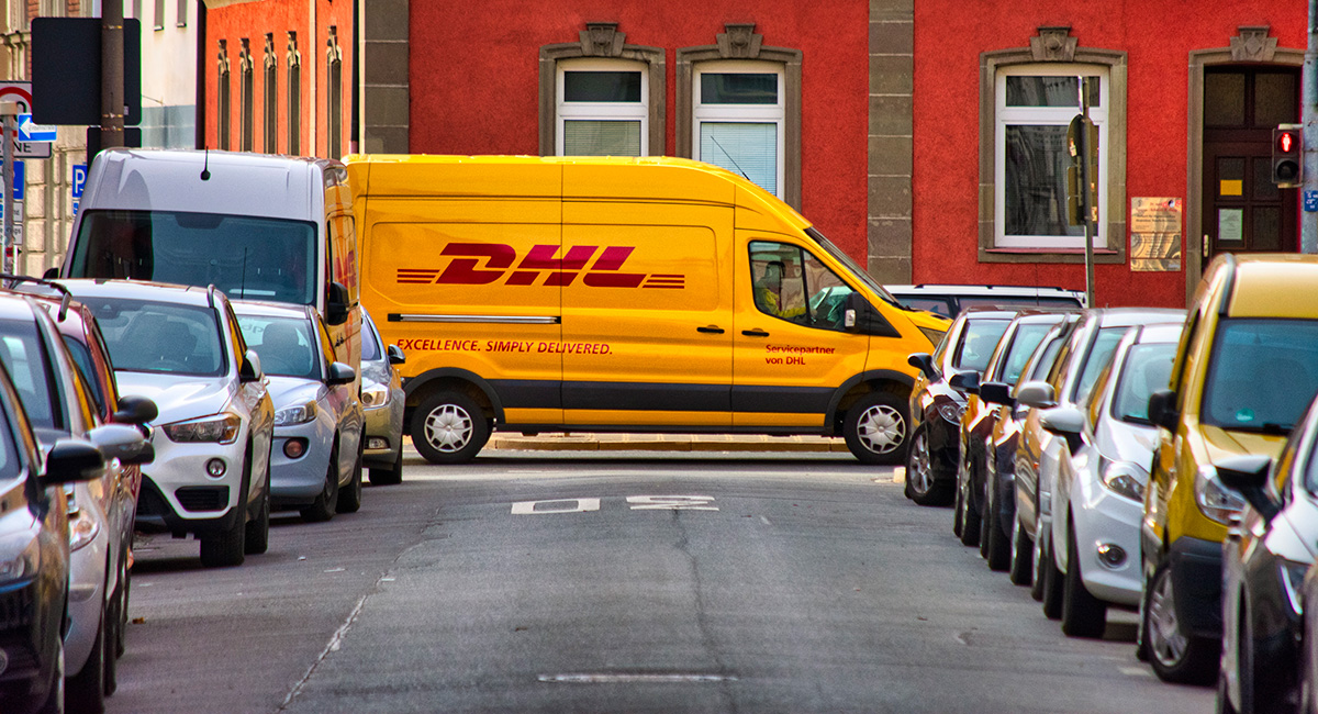 Ein DHL-Van quert eine zugeparkte Straße in der Innenstadt.