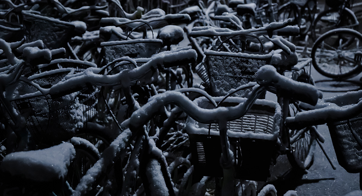 Schneebedeckte Fahrräder stehen in der Dunkelheit in einer Abstellanlage.
