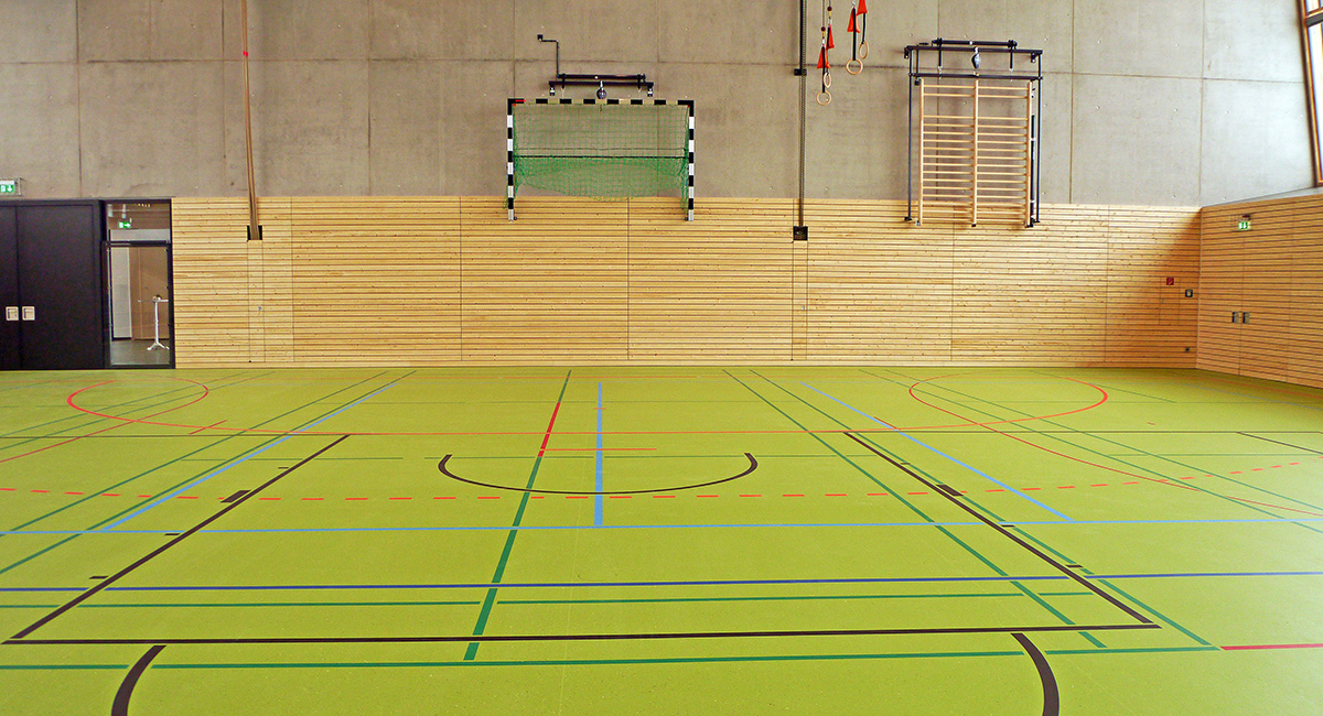 Eine leere Sporthalle mit grünem Hallenboden und vielen Markierungen darauf.