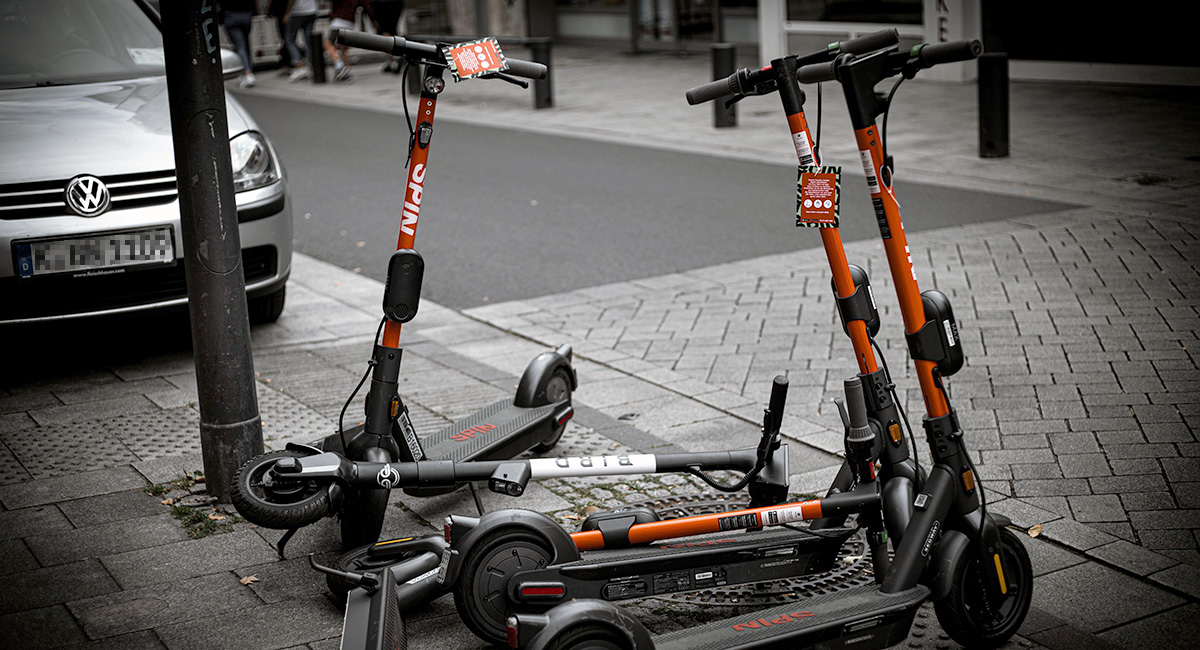 Mehrere orangefarbene E-Leihroller stehen und liegen am Straßenrand.