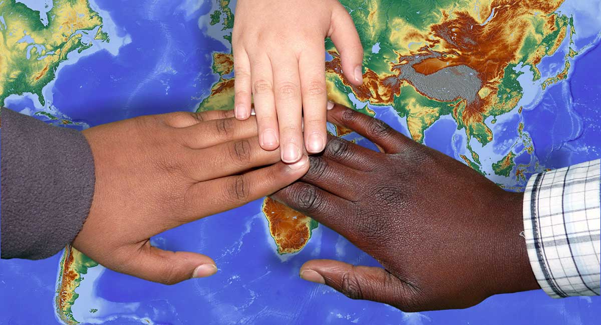 Drei Hände von Menschen unterschiedlicher Hautfarbe über einer Weltkarte.