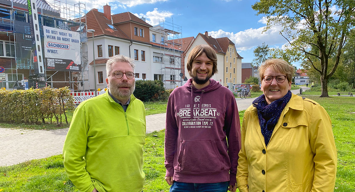 Grüne Ratsmitglieder Petra Tebbe, Björn Engel und Johannes Menze vor eingerüsteten Häusern im Riemekepark.