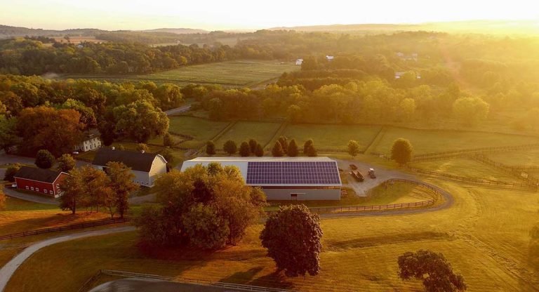 Eine Scheune inmitten einer hügeligen Landschaft. Sie trägt eine große PV-Anlage auf dem Dach und wird von der Abendsonne beschienen.