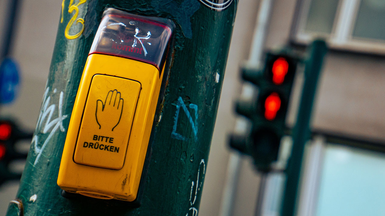 Eine Fußgängerampel mit gelbem Anforderungstaster und Aufschrift „Bitte drücken“.