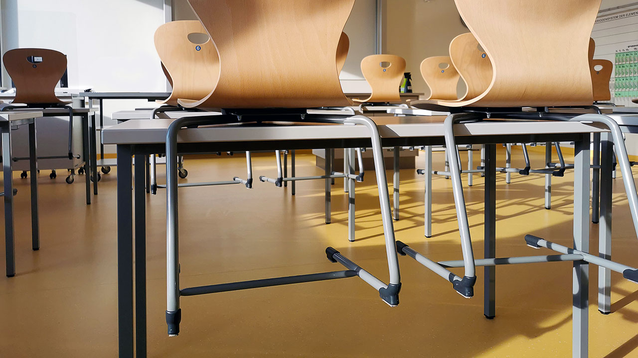 Ein Klassenraum mit vielen Tischen und hochgestellten Stühlen.