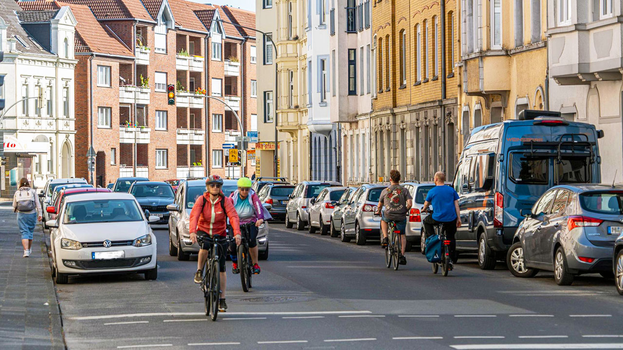 Mehrere Fahrradfahrer*innen, die sich auf einer unübersichtlichen Straße im Riemekeviertels bewegen.