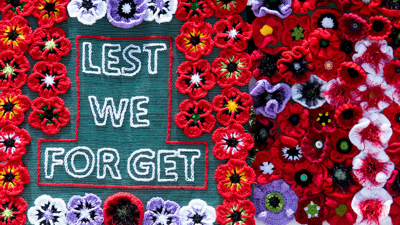 Ein Stoff mit gehäkelten roten Blumen und der Aufschrift „Lest we forget” (wir vergessen nicht).