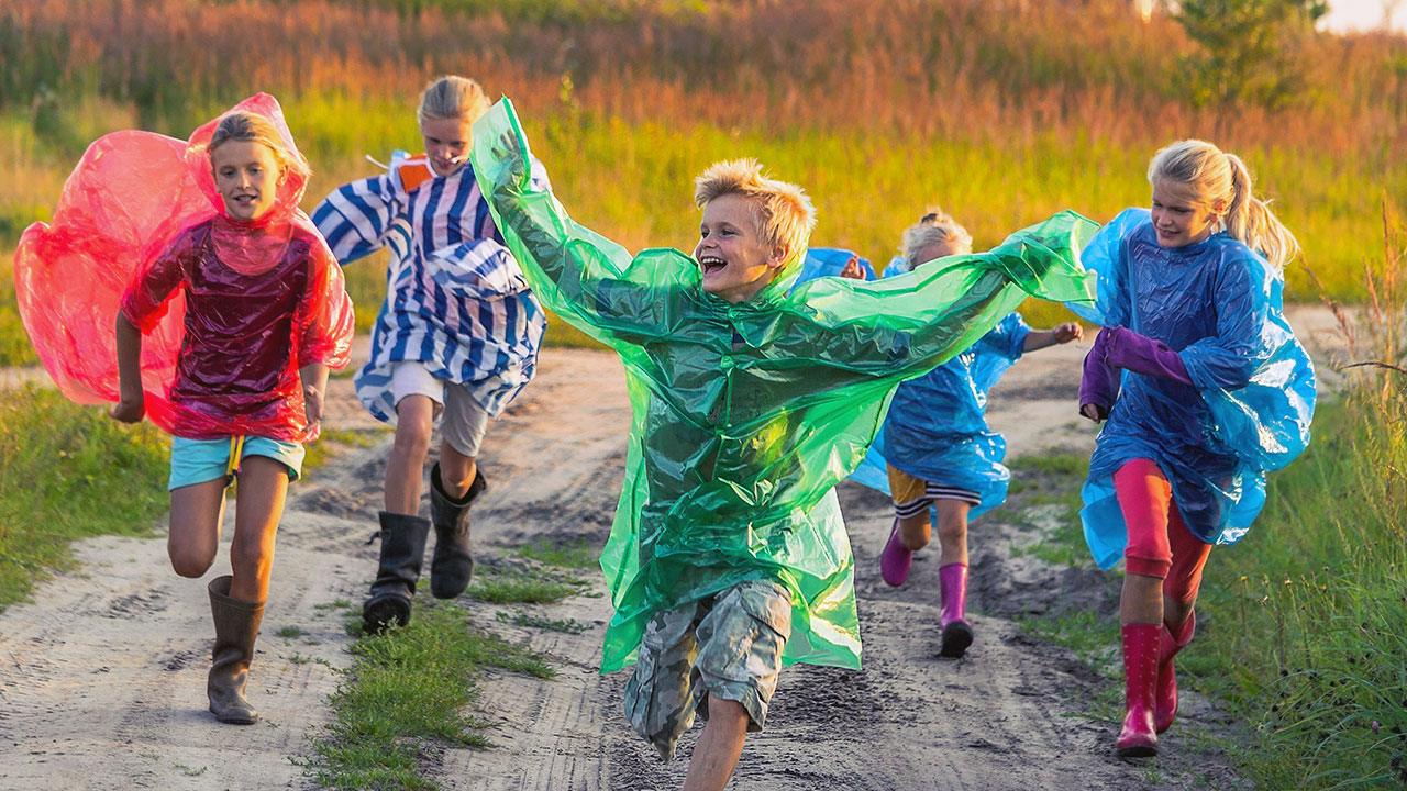 Kinder in bunten Regenmänteln laufen über eine Wiese.