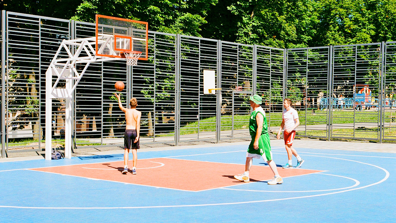 Drei Jugendliche spielen Basketball auf einer Anlage im Freien.