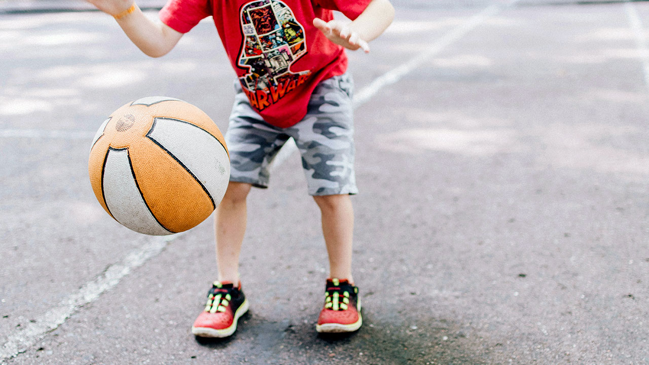 Ein Kind spielt auf einer asphaltierten Fläche mit einem Basketball.