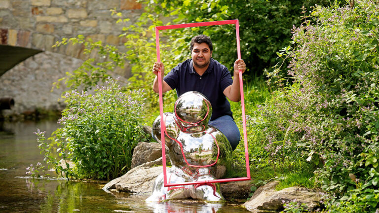 Ratsherr Güven Erkurt mit dem pinkfarbenen Wahlkampagnen-Rahmen hinter einem Kunstwerk von Manfred Webel: einer in der Pader installierten Bubble aus hochglänzendem Edelstahl.