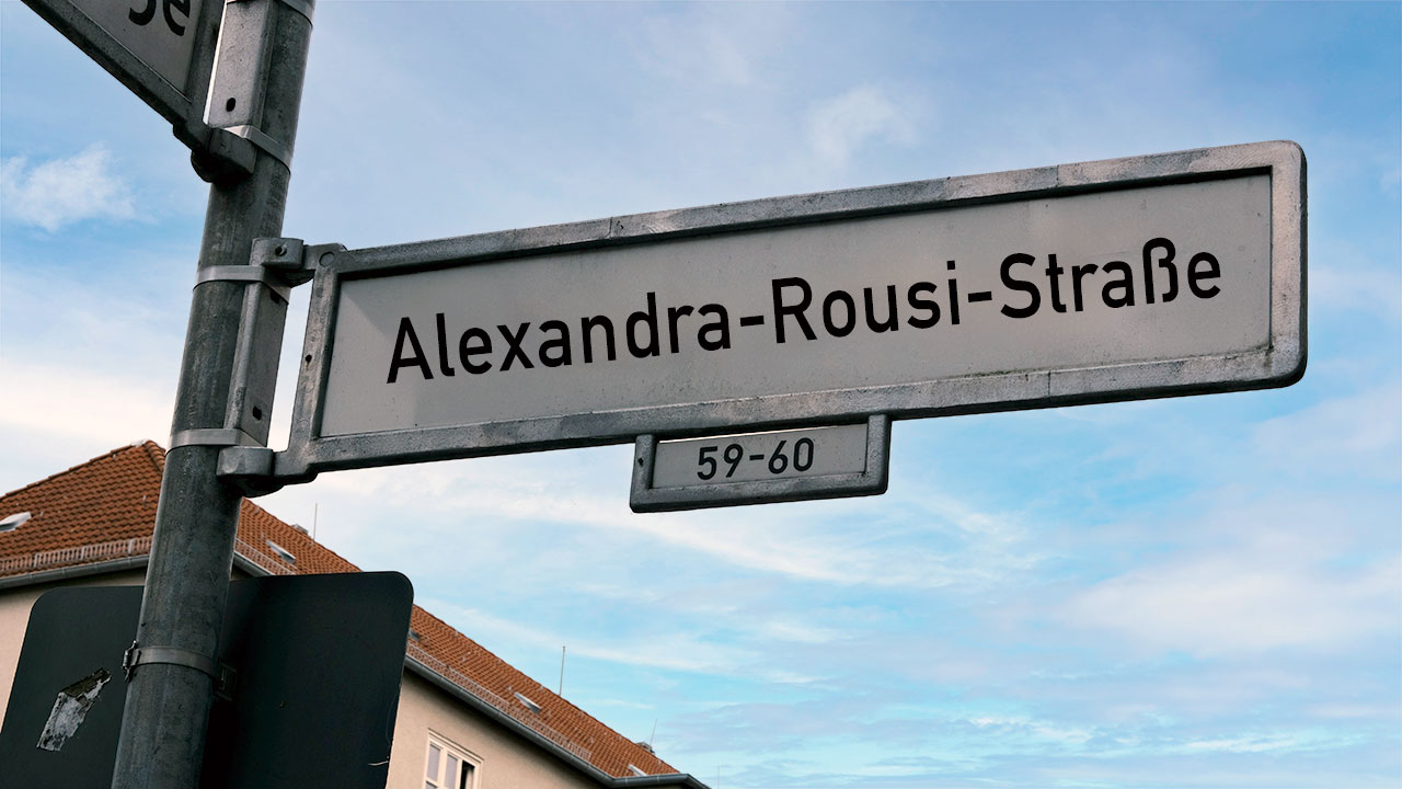 Straßenschild mir der Aufschrift „Alexandra-Rousi-Straße“ vor blauem Himmel.
