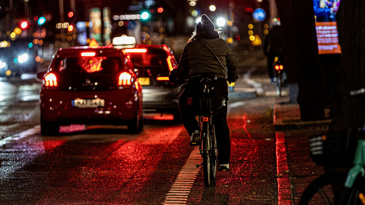 Eine Radfahrerin auf einem Radstreifen, die von Autos dicht überholt wird.
