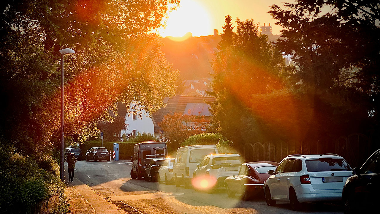 Mehrere Autos parken an einer abschüssigen Straße in einem Wohnviertel.