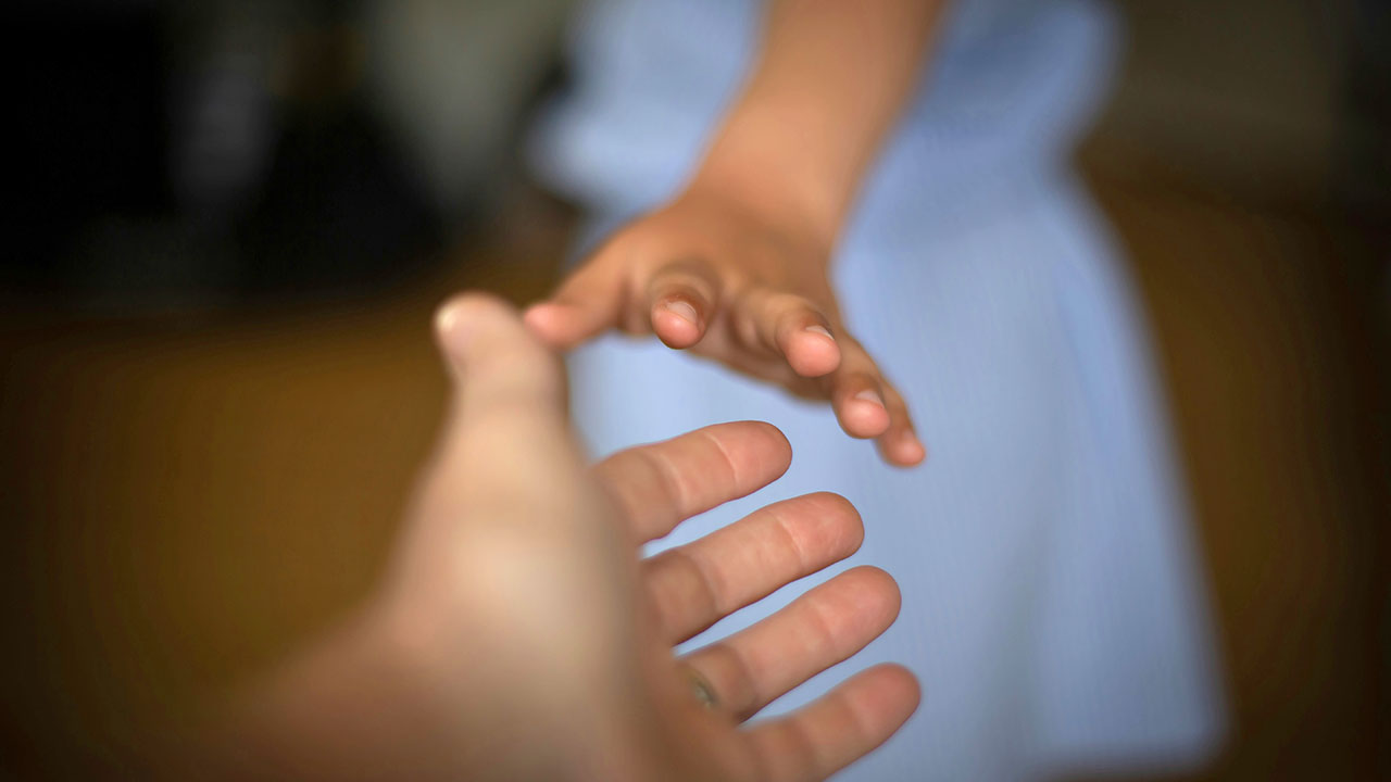 Eine Kinderhand greift nach der Hand eines Erwachsenen.